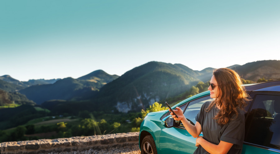 Young beautiful woman traveling by car in the mountains using smartphone at sunset, summer vacation and adventure