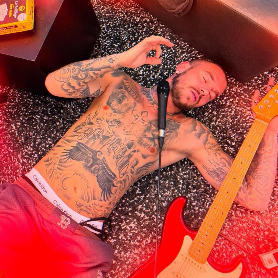 A heavily tattooed man lying on the ground with a microphone and red electric guitar.